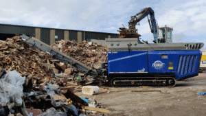 wood shredder breaking down logs and waste near log stacker in BC yard